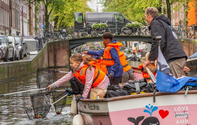 Children fishing plastic in a canal from a pink boat