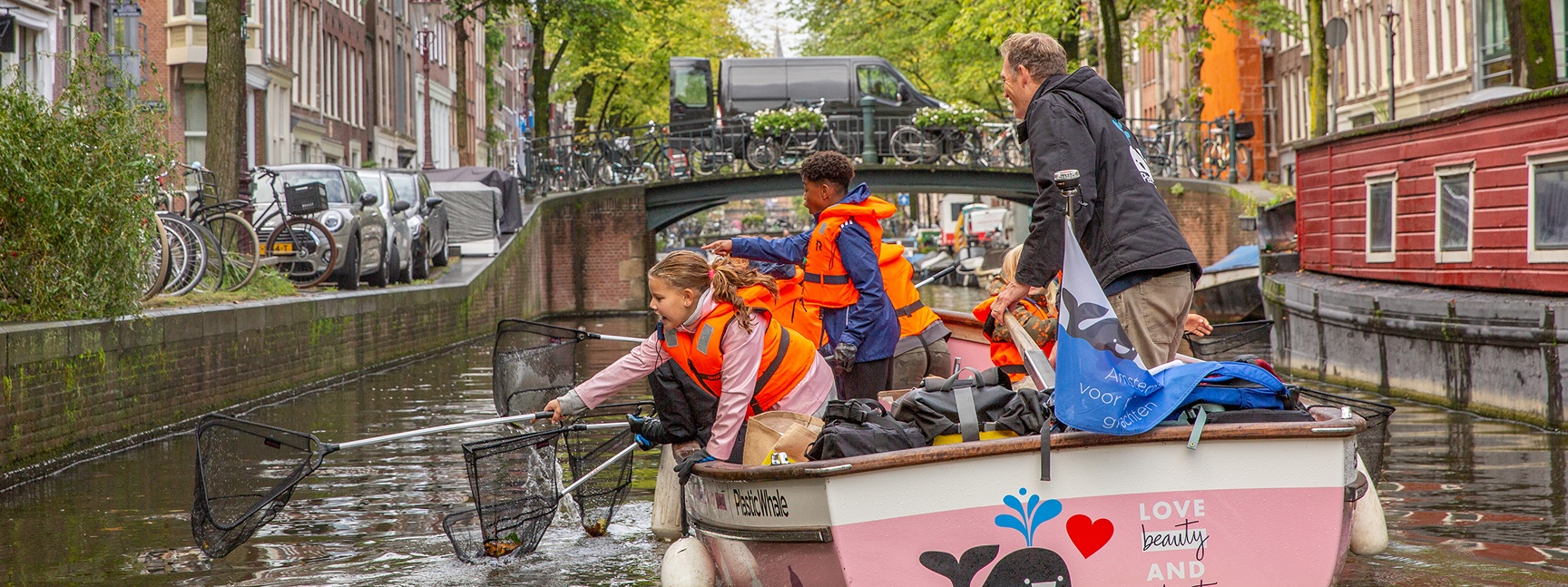 Children fishing plastic in a canal from a pink boat